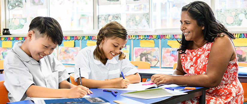 “students-and-teacher-at-desk-in-classroom“