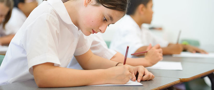 “student-working-at-desk-in-classroom“class="img-fluid"