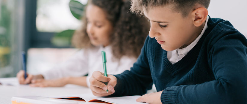 “student-writing-at-desk-in-classroom“