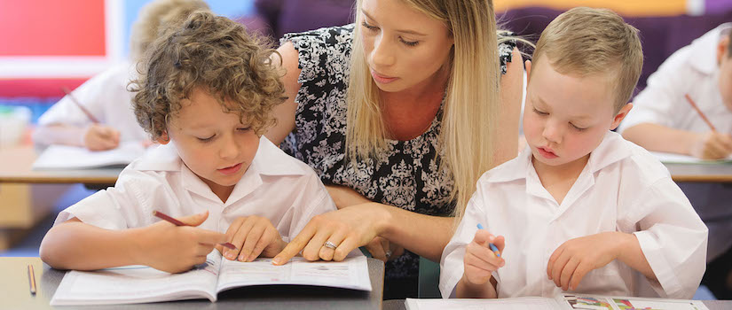 “teacher-at-desk-with-students-in-classroom“