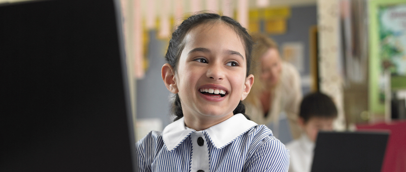 “student-smiling-at-desk-in-classroom“