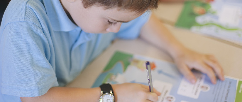 “student-using-writing-time-book-at-desk-in-classroom“