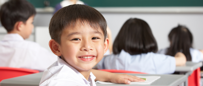 “student-smiling-at-desk-in-classroom“