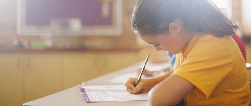 “student-writing-at-desk-in-classroom“class="img-fluid"