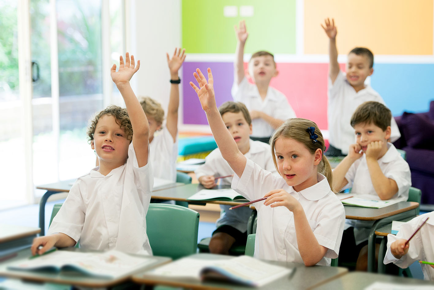 students at desk raising hands to answer question